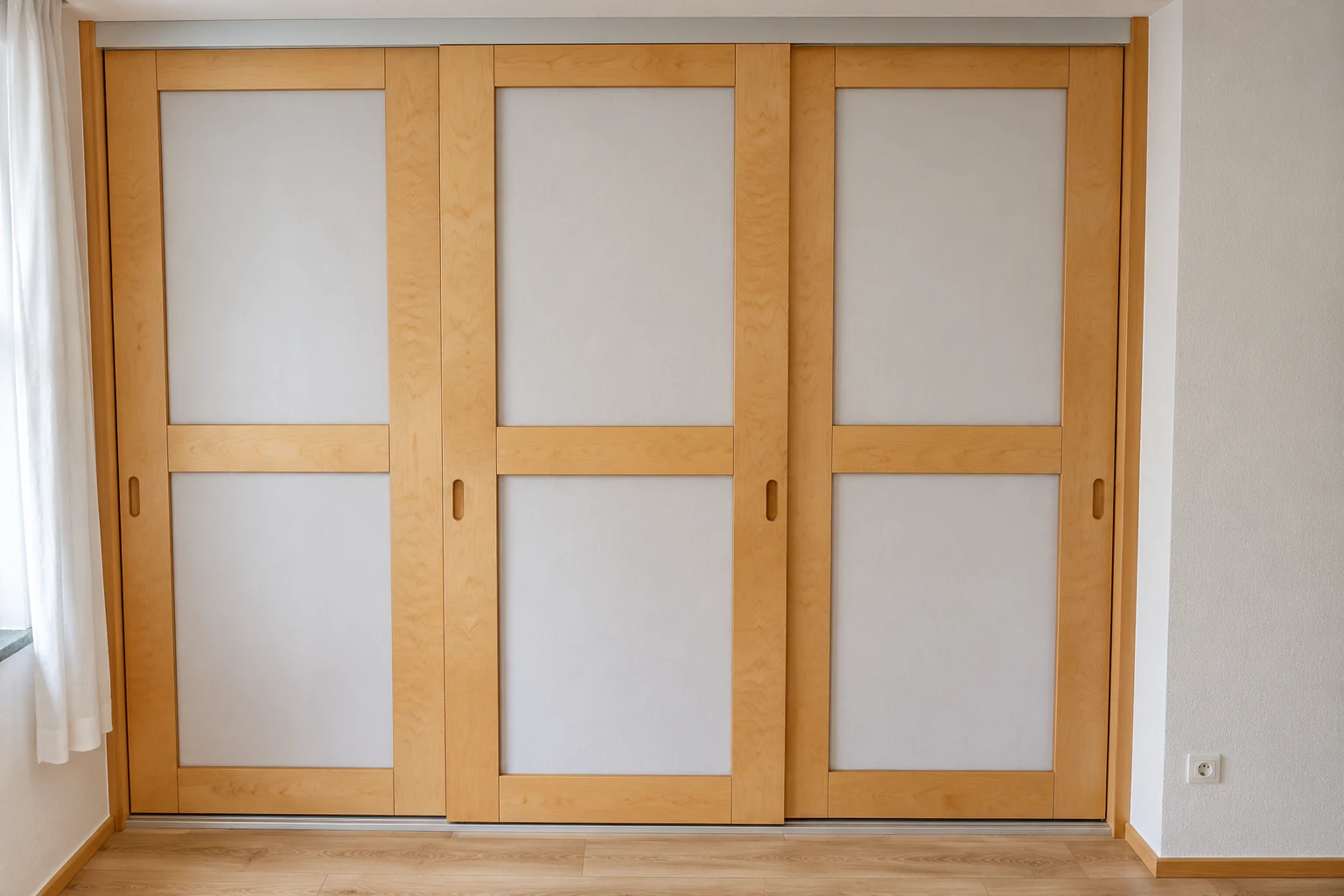 Dreiteiliger Schiebetürenschrank aus hellem Holz.